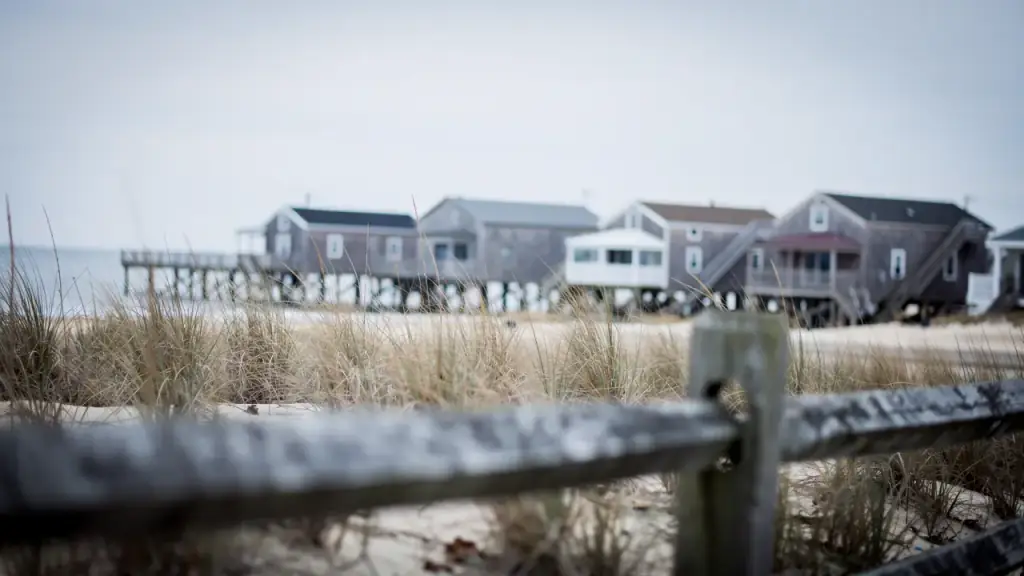 Raised shingled cottages on pilings along the bay, beach grass and a split-rail fence in the foreground