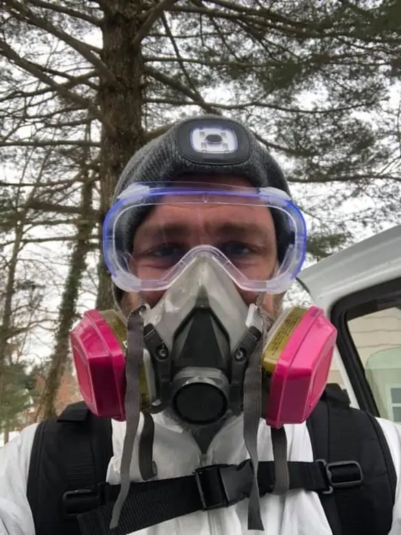 Technician in a respirator, goggles and white protective suit with a treatment backpack
